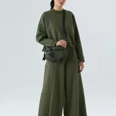 Conjunto verde-oliva com camisola e calças largas, mala preta e ténis escuros