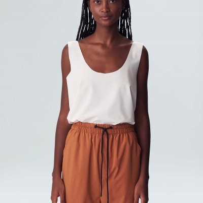 Mulher vestindo blusa branca de alças largas e calças castanhas com cordão.