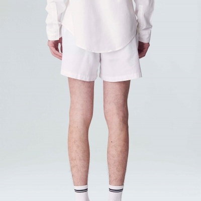 Vista de trás de um homem com camisa branca, shorts brancos, meias brancas com risca preta e sapatilhas bege, preto e vermelho