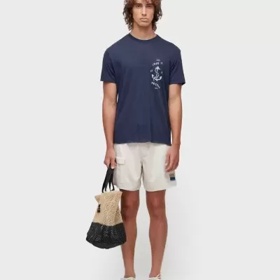 Homem com t-shirt azul escura, calções bege, sapatilhas brancas e mala de rede bicolor bege e preta