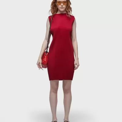 Mulher com vestido vermelho justo sem mangas e acessórios em fundo branco.