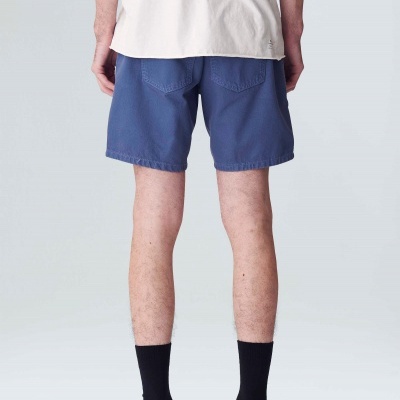 Pessoa de costas com calções azuis, t-shirt branca, meias pretas e sapatos pretos/bege