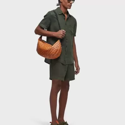 Homem com roupa verde, ténis verdes com detalhes laranja e mala castanha entrelaçada