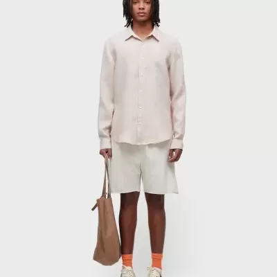 Homem com camisa bege, calções brancos, meias laranja, ténis e mala castanha