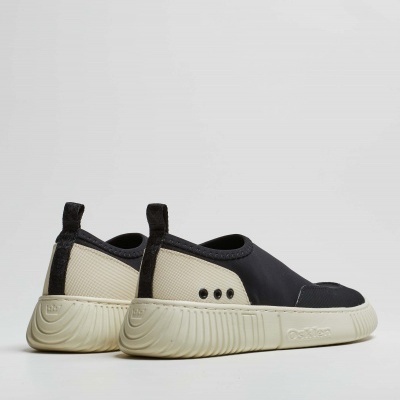 Ténis slip-on preto e creme sobre fundo cinza claro