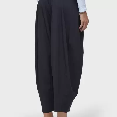 Calças pretas largas e fluídas com cintura alta, usadas com camisola branca e ténis brancos.