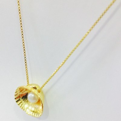 Colar dourado com concha e pérola sobre fundo branco