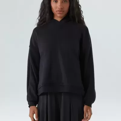 sweatshirt preta com capuz de tecido liso e saia preta num fundo claro