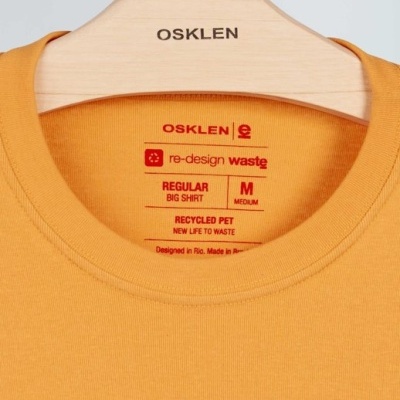 T-shirt laranja com etiqueta vermelha pendurada em cabide de madeira OSKLEN