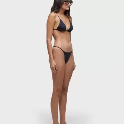 Mulher com biquíni preto de duas peças e óculos escuros em fundo branco.