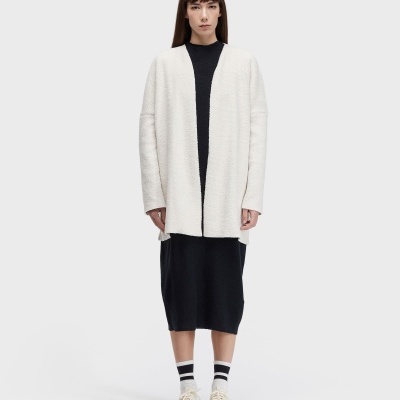 Mulher com casaco branco e vestido preto, fundo cinza claro