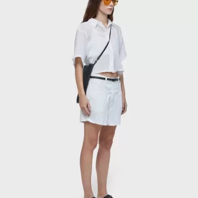 Mulher com camisa branca, saia branca, sandálias pretas e óculos de sol amarelos