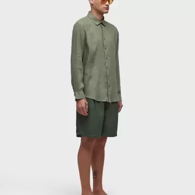 Homem vestido com camisa, calções e chinelos verdes, usando óculos de sol castanhos.