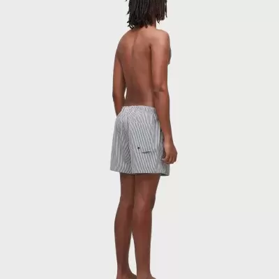 Homem de costas a usar calções de banho risca preta e branca e chinelos pretos