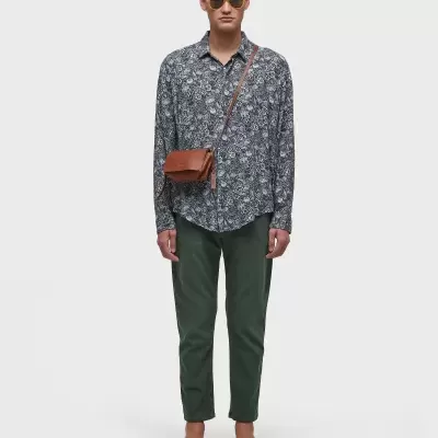 Homem com camisa padrão, calças verdes e mala castanha