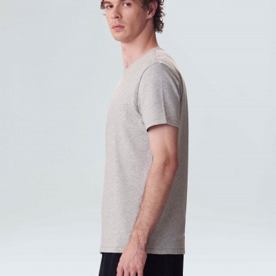 Homem de perfil com t-shirt cinzenta e calças pretas em fundo branco.