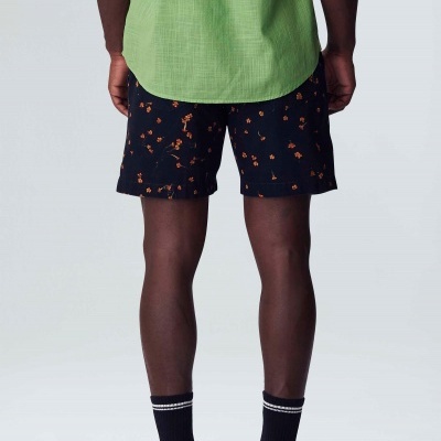 Homem de costas com camisa verde, calções pretos com flores laranja, meias pretas e sapatos pretos