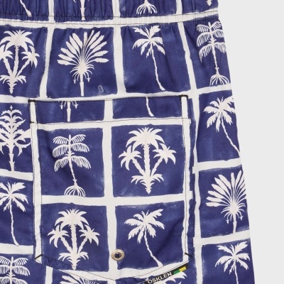 Pormenor de roupa azul com padrão de palmeiras brancas e bolso com etiqueta OSKLEN
