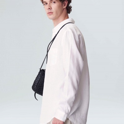 Homem com camisa branca, calças claras e bolsa preta texturada