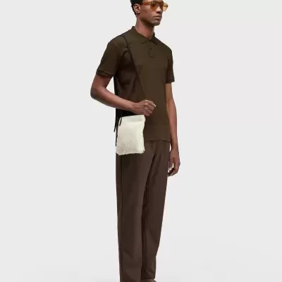 Homem com polo e calças castanhas, sandálias e bolsa branca de pelo