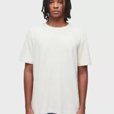 T-shirt branca de manga curta com gola redonda, usada por modelo, com calças de ganga azuis.