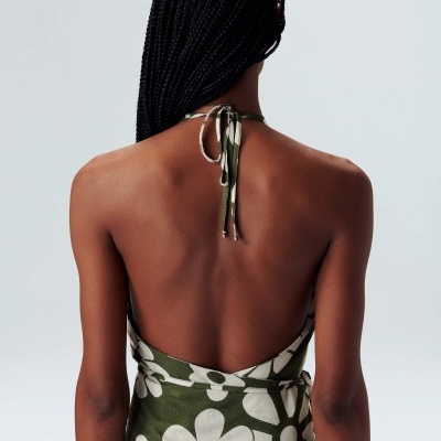 Mulher de costas veste vestido verde com flores brancas e cabelo trançado