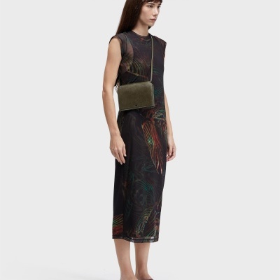 Mulher com vestido estampado, bolsa verde e sandálias castanhas