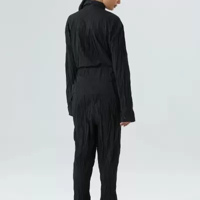 Macacão preto texturizado visto de costas com fundo cinza claro