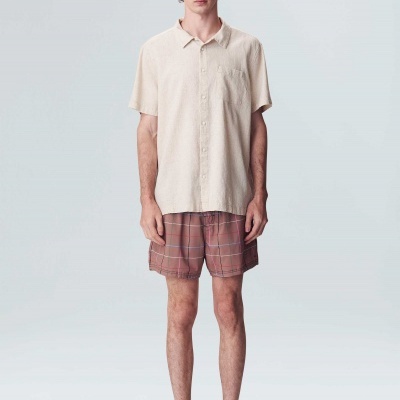 Homem com camisa bege de manga curta e calções castanhos xadrez