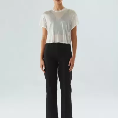 Mulher com blusa branca transparente, calças pretas, sandálias e óculos de sol