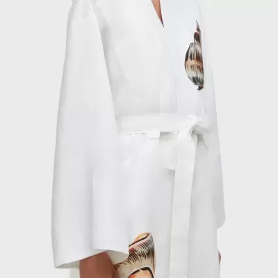 Casaco branco com estampas de conchas e cinto no peito e na zona inferior, detalhes das mangas largas.