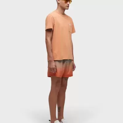 Homem com t-shirt pêssego, calções degradê laranja e sapatos brancos