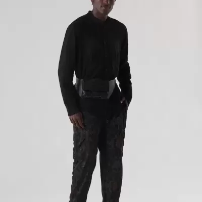 Homem com camisa preta, calças cargo camufladas pretas, sapatos brancos e pochete preta