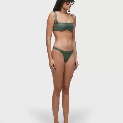 Modelo usa bikini verde-escuro com óculos escuros e sandálias pretas em fundo cinza claro