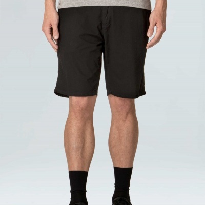 Homem com bermuda preta, camiseta cinza, meias e ténis pretos em fundo neutro