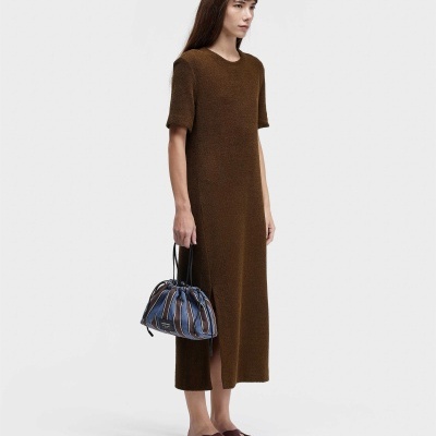 Mulher com vestido castanho e bolsa azul com riscas a posar em fundo branco