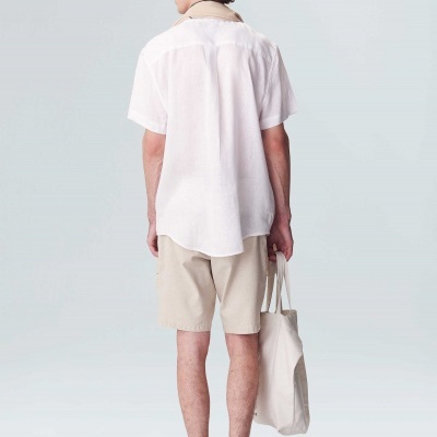 Homem de costas com camisa branca e calções bege segurando mala de tecido