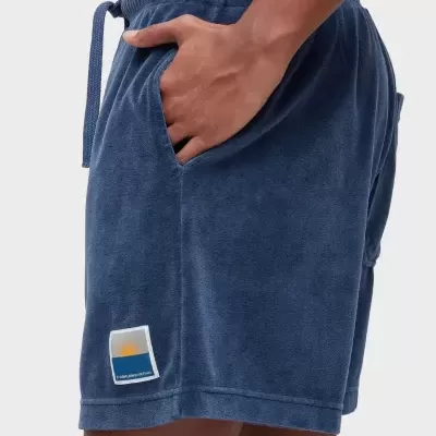 Calções azuis felpudos com bolso e etiqueta com sol e texto OAKLEINSURFING