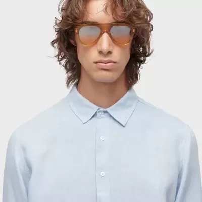 Homem com óculos de sol castanhos translúcidos e camisa azul clara
