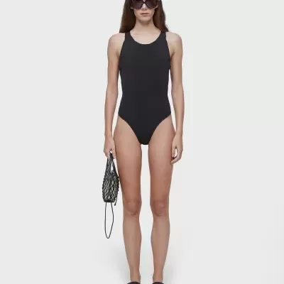 Mulher com fato de banho preto e óculos, segurando bolsa preta de malha