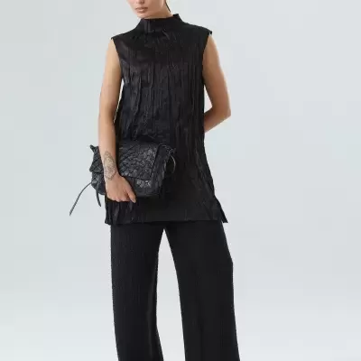 Mulher com roupa preta e bolsa preta em fundo branco