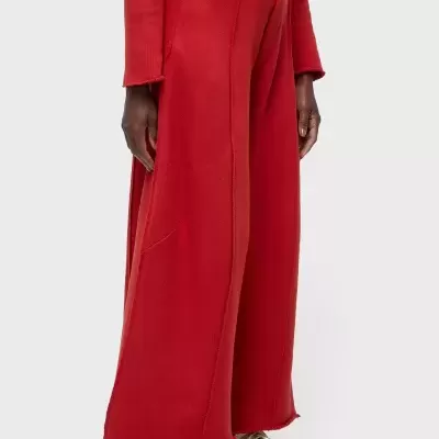 Calças largas vermelhas com costuras visíveis e barra desfiada, usadas com camisola vermelha e sapatilhas brancas com sola vermelha.