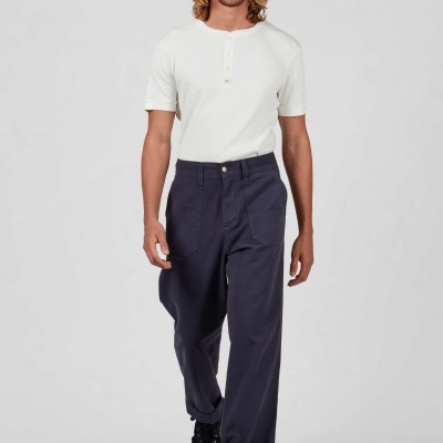 Homem com t-shirt branca de manga curta e calças largas azul escuro, em fundo cinza