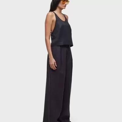 Mulher com top preto, calças largas pretas e óculos de sol amarelos em fundo cinza.