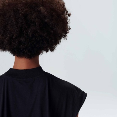 Pessoa vista de costas com t-shirt preta sem mangas e cabelo encaracolado
