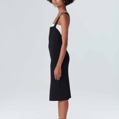 Mulher com vestido preto e camisola branca, meias riscas e tênis brancos em fundo branco