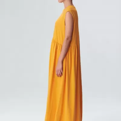 Vestido amarelo comprido e sem mangas usado por modelo em fundo branco.