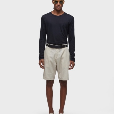 Homem com roupa casual preta e bege, óculos de sol, fundo cinza claro