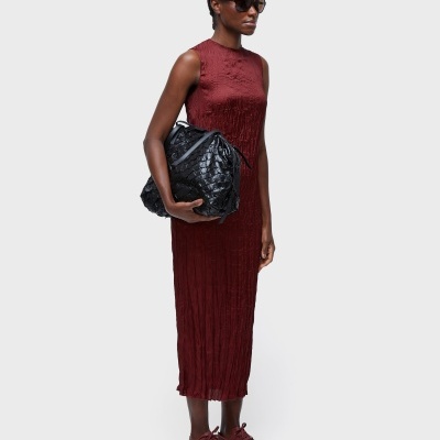 Mulher com vestido vinho longo, óculos escuros, sapatilhas vinho e mala preta com padrão de relevo