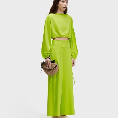 Mulher vestida com conjunto verde lima e segurando mala bege acolchoada